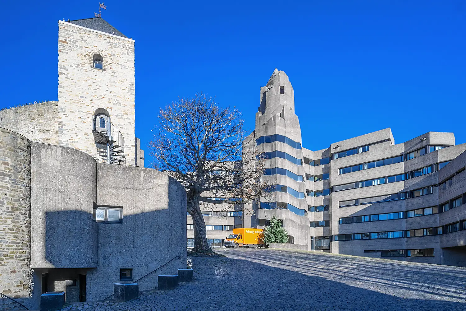 Das Bensberger Rathaus von Gottfried Böhm aus Sichtbeton, links der Bergfried der Burg, unter blauem Himmel