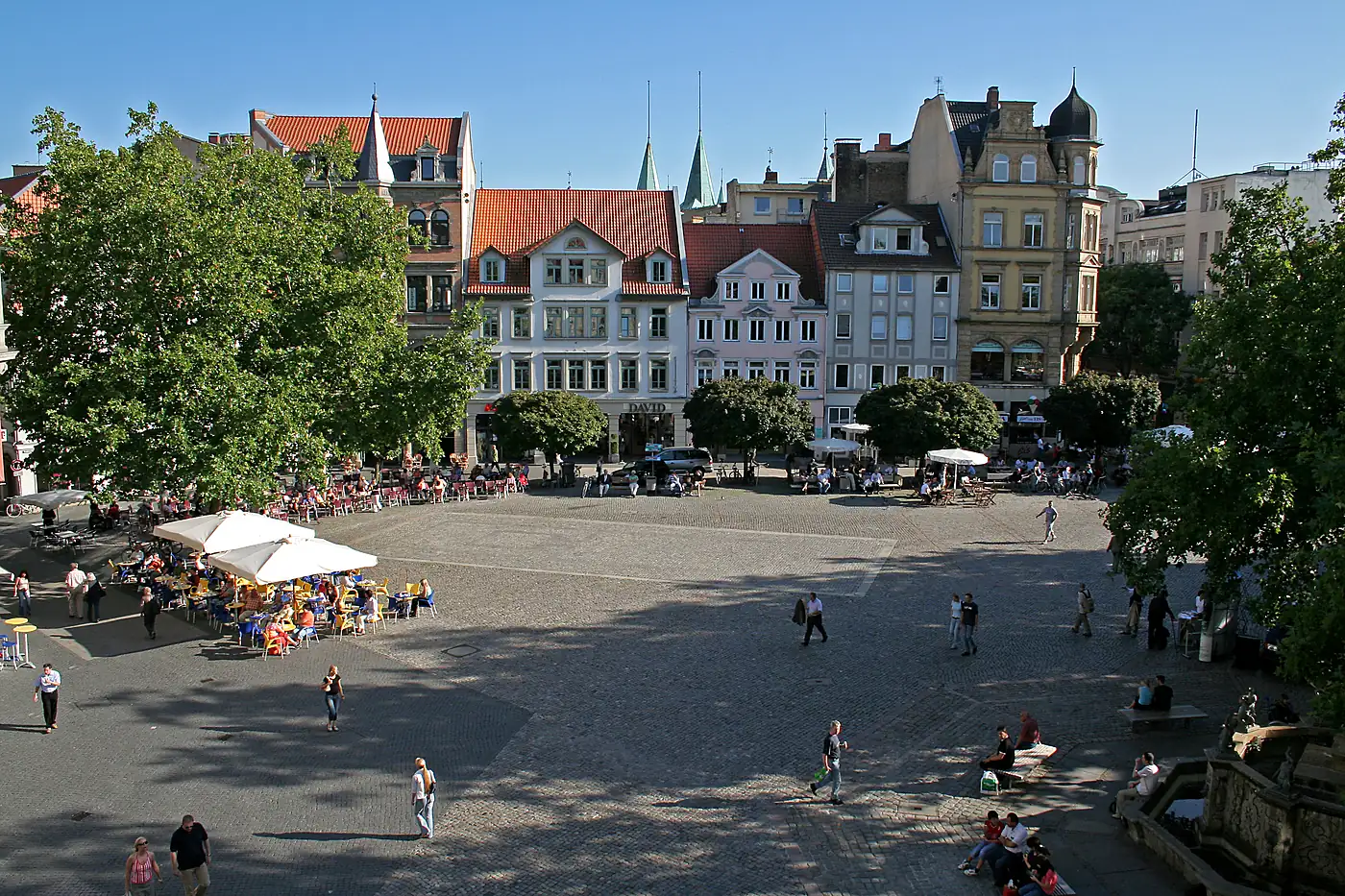 Kohlmarkt in Braunschweig mit Café-Tischen unter Bäumen, dahinter Bürgerhäuser und zwei Kirchturmspitzen