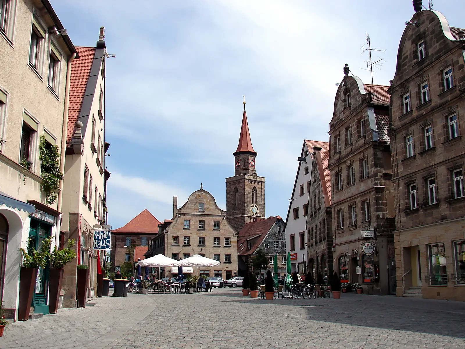 Marktplatz in der Fürther Altstadt mit Sandsteinhäusern, einem roten Kirchturm und Cafétischen