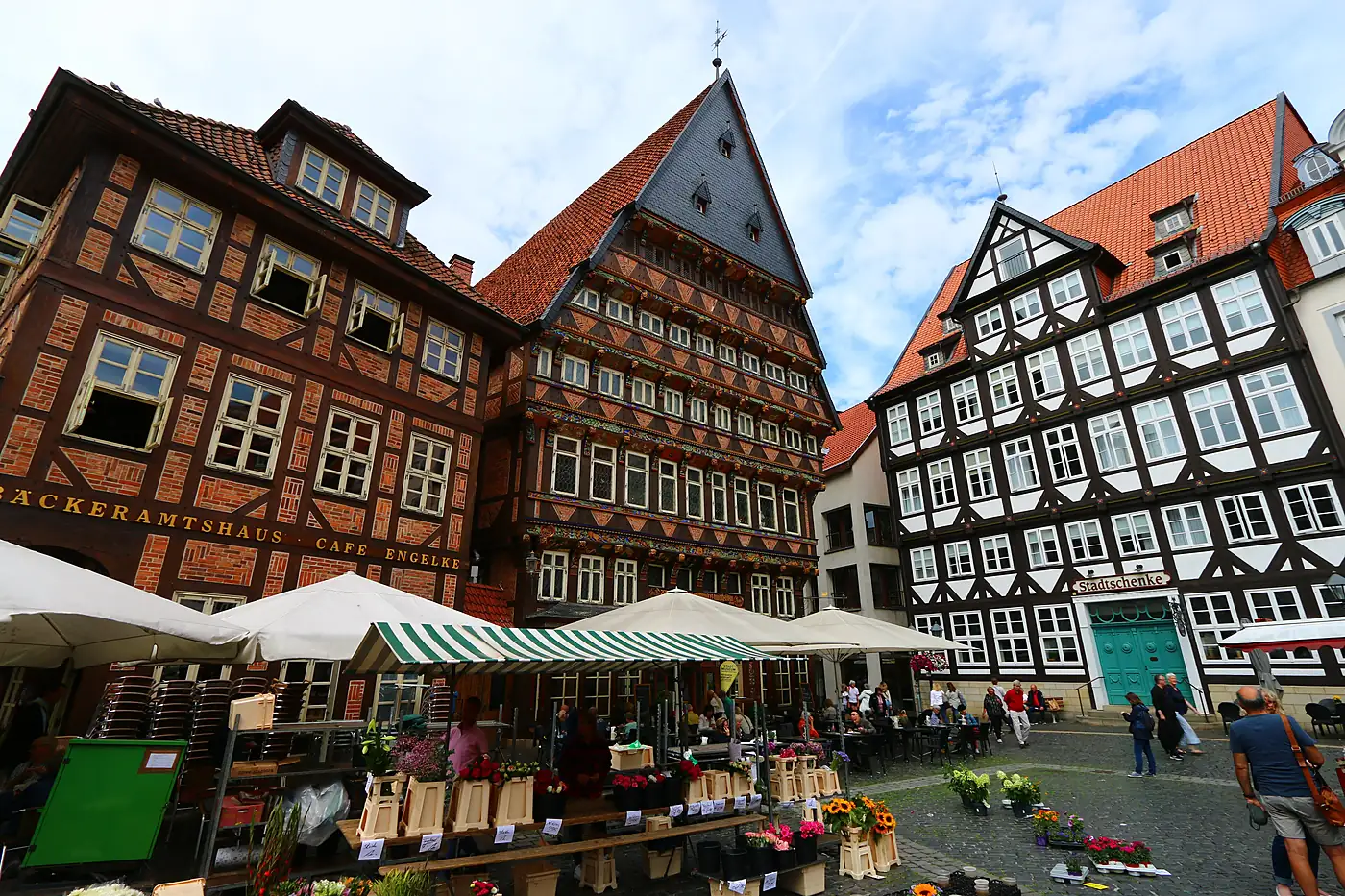 Marktplatz in Hildesheim mit dem Knochenhaueramtshaus und weiteren Fachwerkhäusern, davor ein Blumenstand und Sonnenschirme