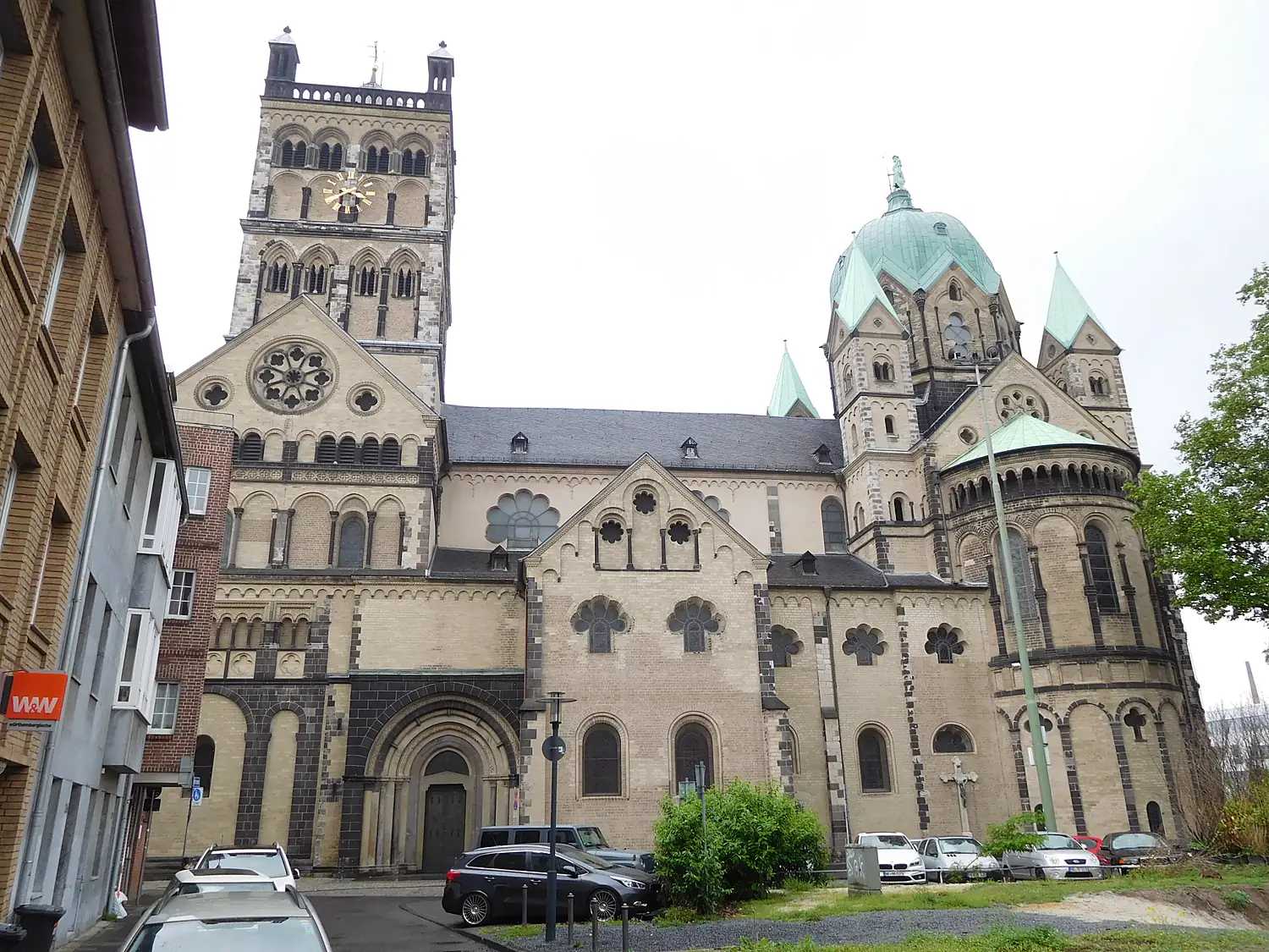 Quirinus-Münster in Neuss, spätromanische Kirche mit Glockenturm, Kupferkuppel und Chorapsis, davor geparkte Autos