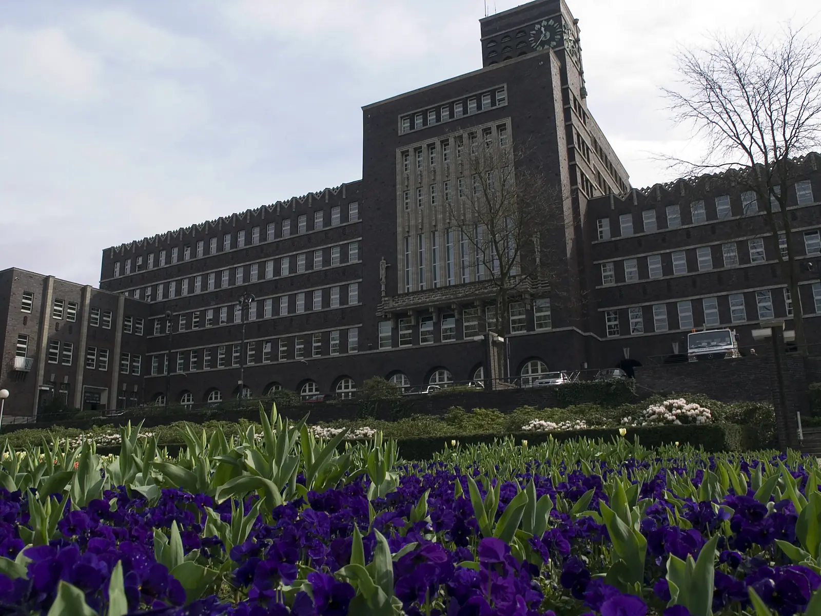Das Rathaus von Oberhausen, ein dunkler Backsteinbau mit hohem Mittelteil, davor ein Beet mit violetten Blumen