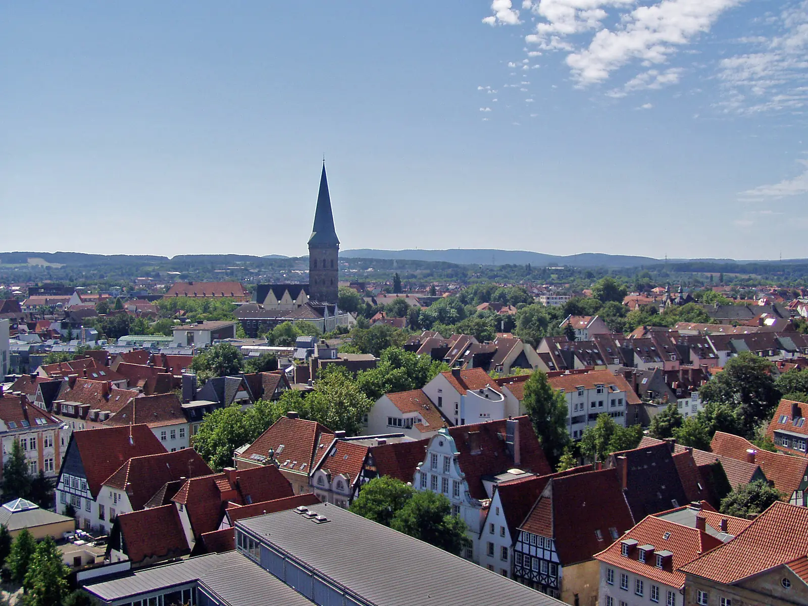 Dächer und Fachwerkhäuser der Osnabrücker Innenstadt mit einem Kirchturm vor bewaldeten Hügeln