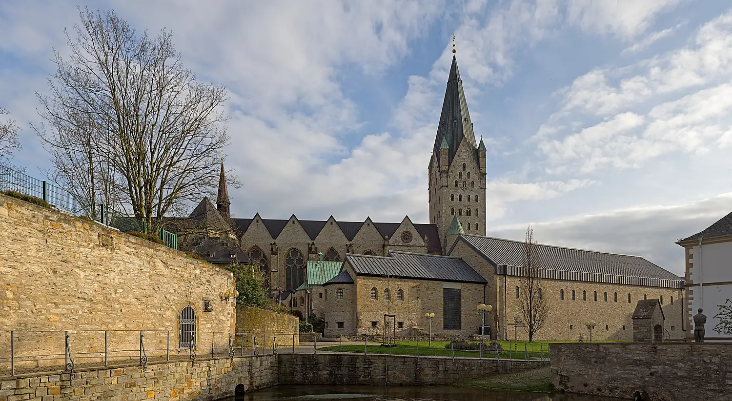 Der Paderborner Dom mit hohem Turm von Norden, davor Bruchsteinmauern, Dächer und Wasser