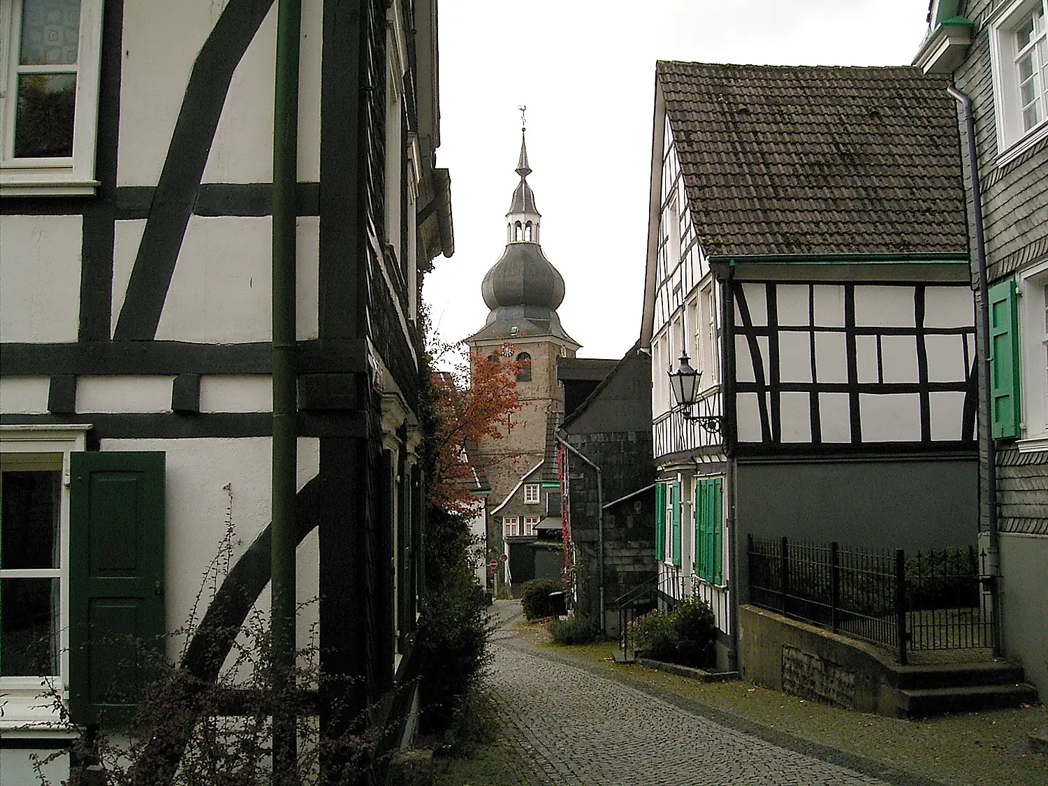 Fachwerkhäuser und Schieferfassaden in einer Gasse der Altstadt von Lennep mit Kirchturm im Hintergrund