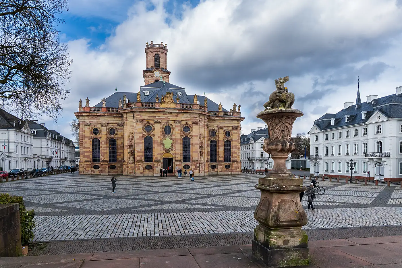 Die barocke Ludwigskirche in Saarbrücken mit Natursteinfassade am gepflasterten Ludwigsplatz, daneben weiße Häuser